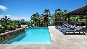 Une piscine entourée de chaises longues, de palmiers et sous un ciel dégagé.