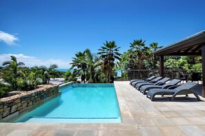 A swimming pool with lounge chairs, surrounded by palm trees and a clear sky. - Infinite Blue (Airlie Beach)