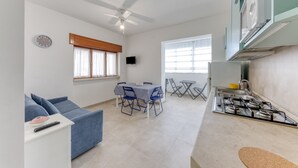 A modern kitchen with a gas stove, a dining area with a table and chairs, a sofa, and a ceiling fan.