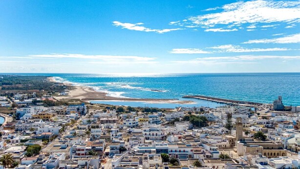 A coastal town with dense housing, a beach, and a clear blue sky.