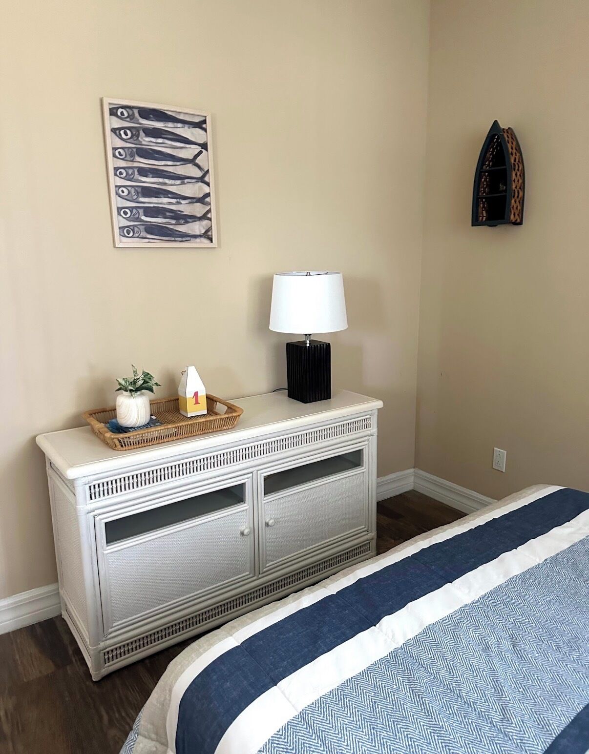 Une chambre à coucher comprenant un lit, une commode, une lampe, une décoration murale représentant des poissons et une petite étagère avec des objets décoratifs.