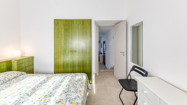 Une chambre à coucher avec un lit, une armoire verte, une commode, une chaise et un miroir.