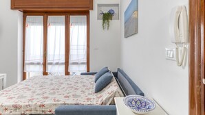 Een slaapkamer met een bed, een nachtkastje, een aan de muur bevestigd telefoon, een raam met gordijnen en een aan de wand hangende plant.