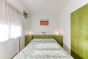 Une chambre à coucher avec un lit, une commode verte, une armoire verte, un tableau accroché au mur et une fenêtre avec des rideaux.