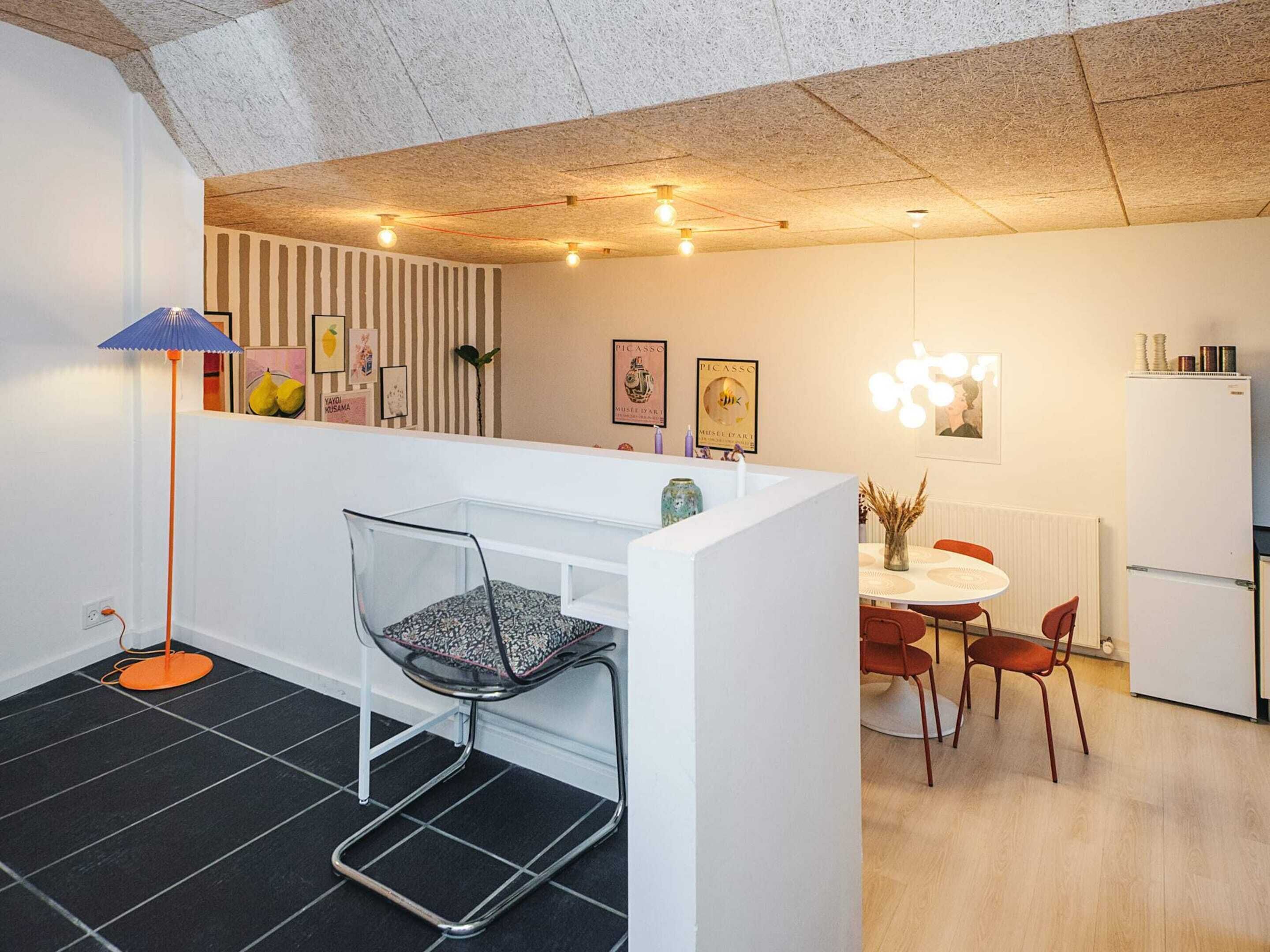 A modern kitchen with a white island, a dining area with a round table and chairs, and a small seating area with a chair and floor lamp.