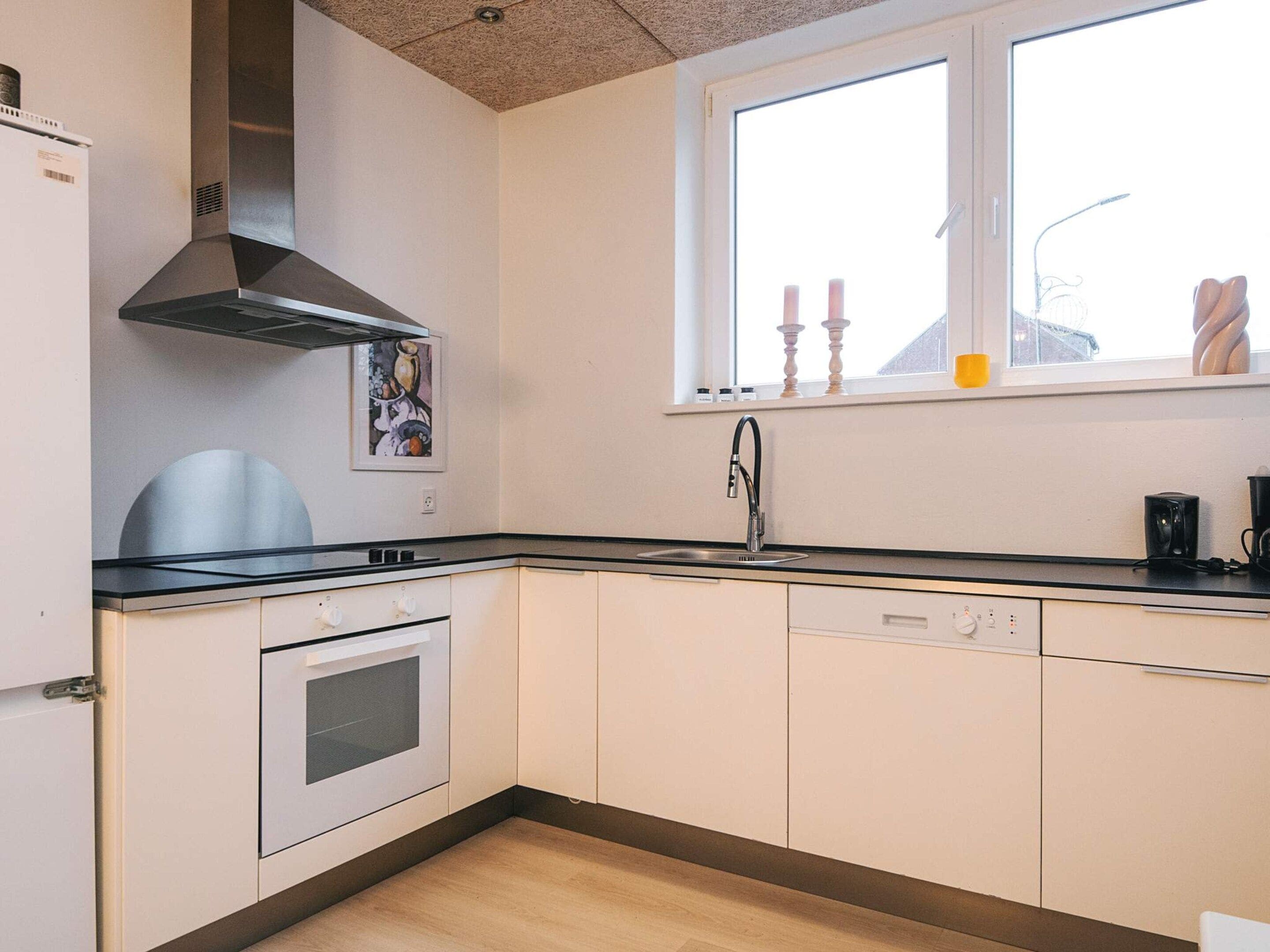 A kitchen with a stove, oven, and sink, a window with a view, and a ceiling vent.
