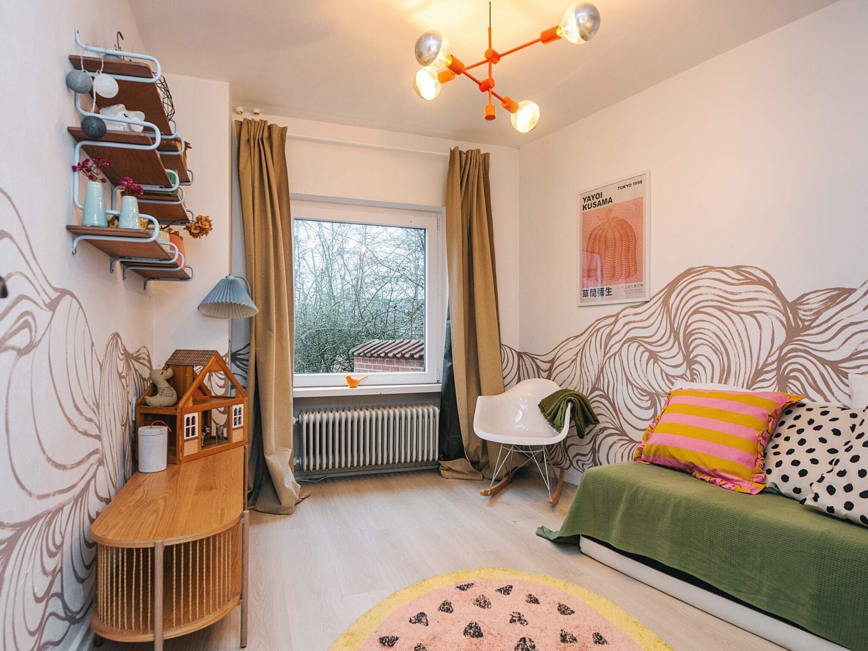 A cozy bedroom with a bed, a radiator, a window with curtains, a wall with a poster, and a shelf with decorative items.