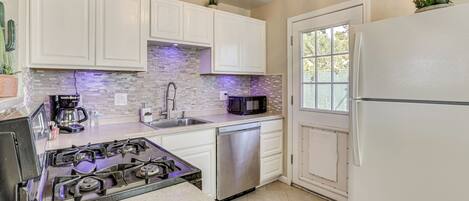 A kitchen with white cabinets, a stainless steel dishwasher, a gas stove, and a refrigerator.