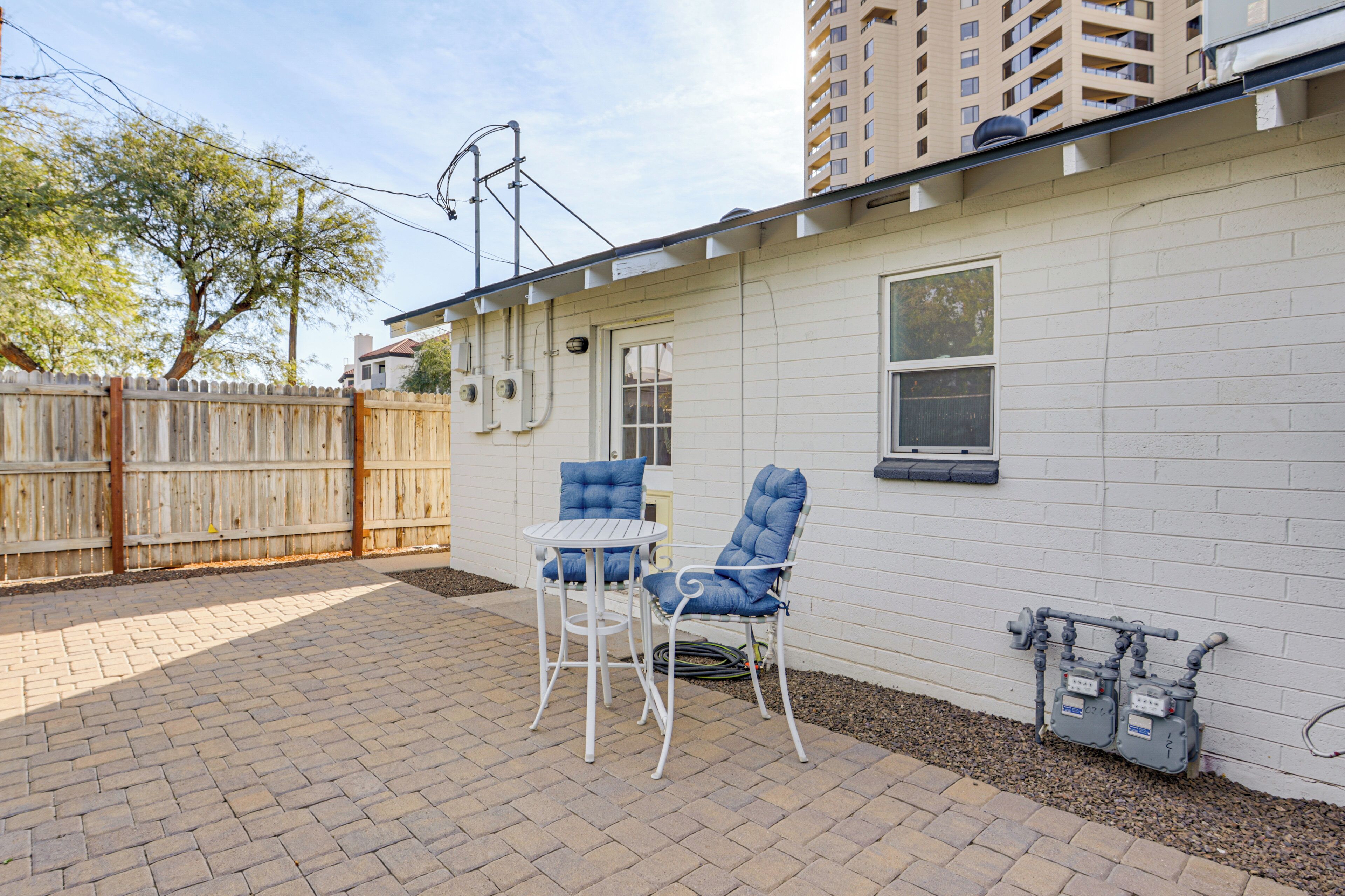 A patio area with a white brick wall, a wooden fence, and two blue chairs.
