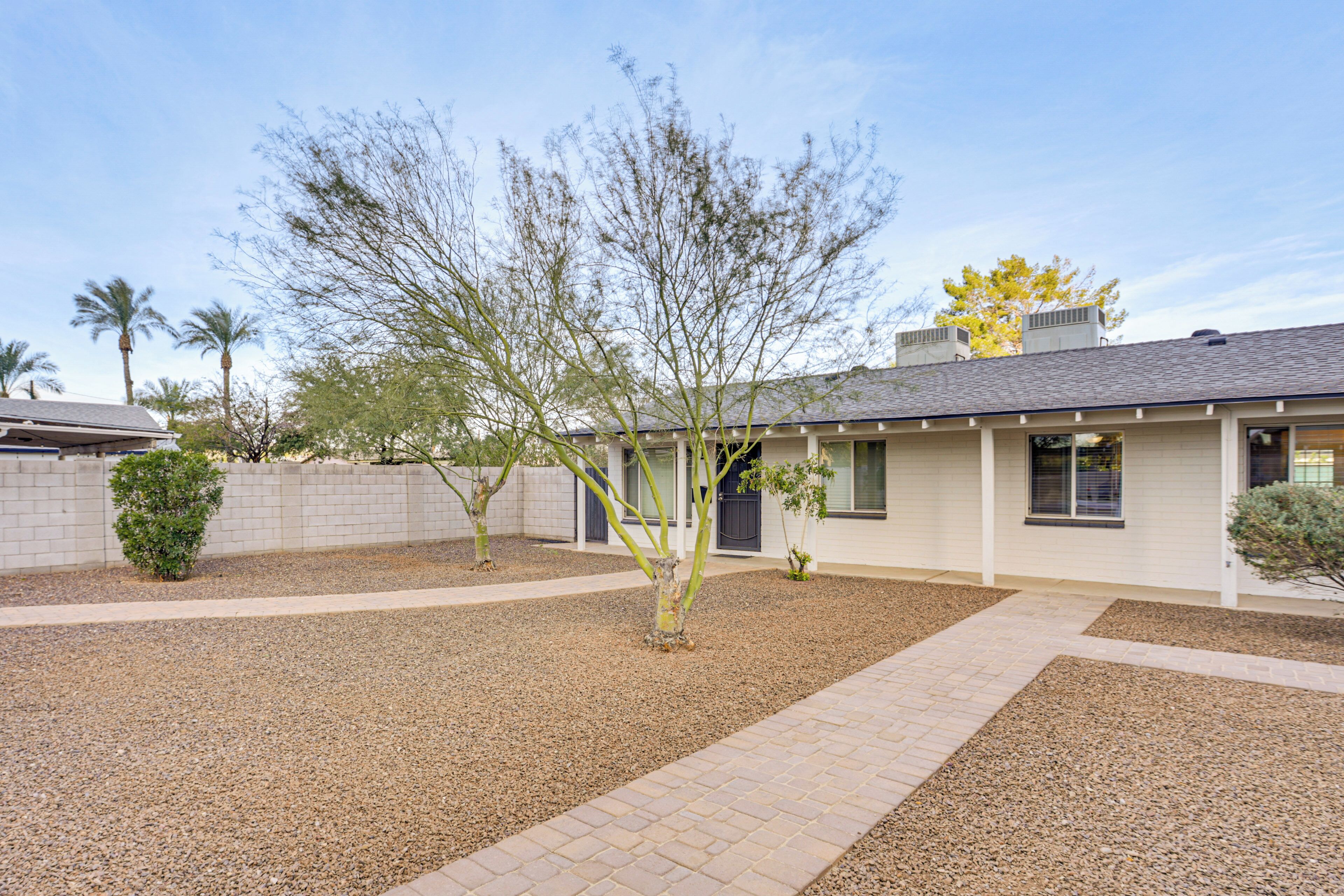 A residential building with a paved driveway, a small garden with a tree, and a white exterior.