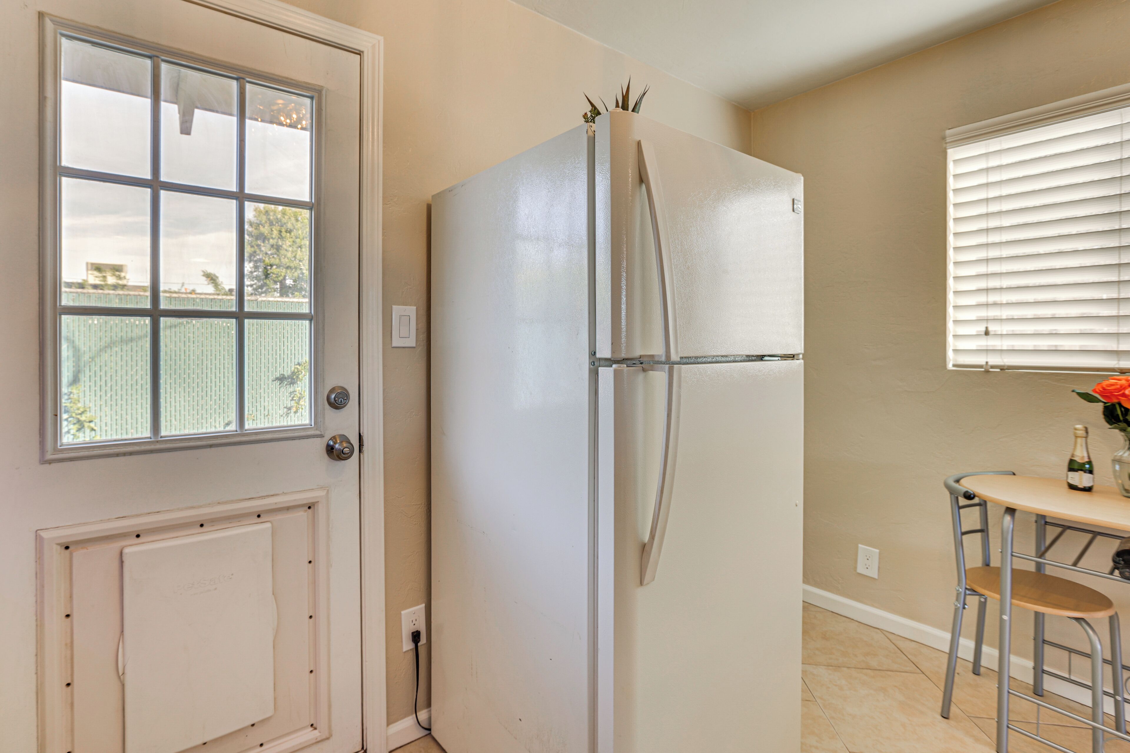 A kitchen with a white refrigerator, a window with blinds, and a small table with a chair.