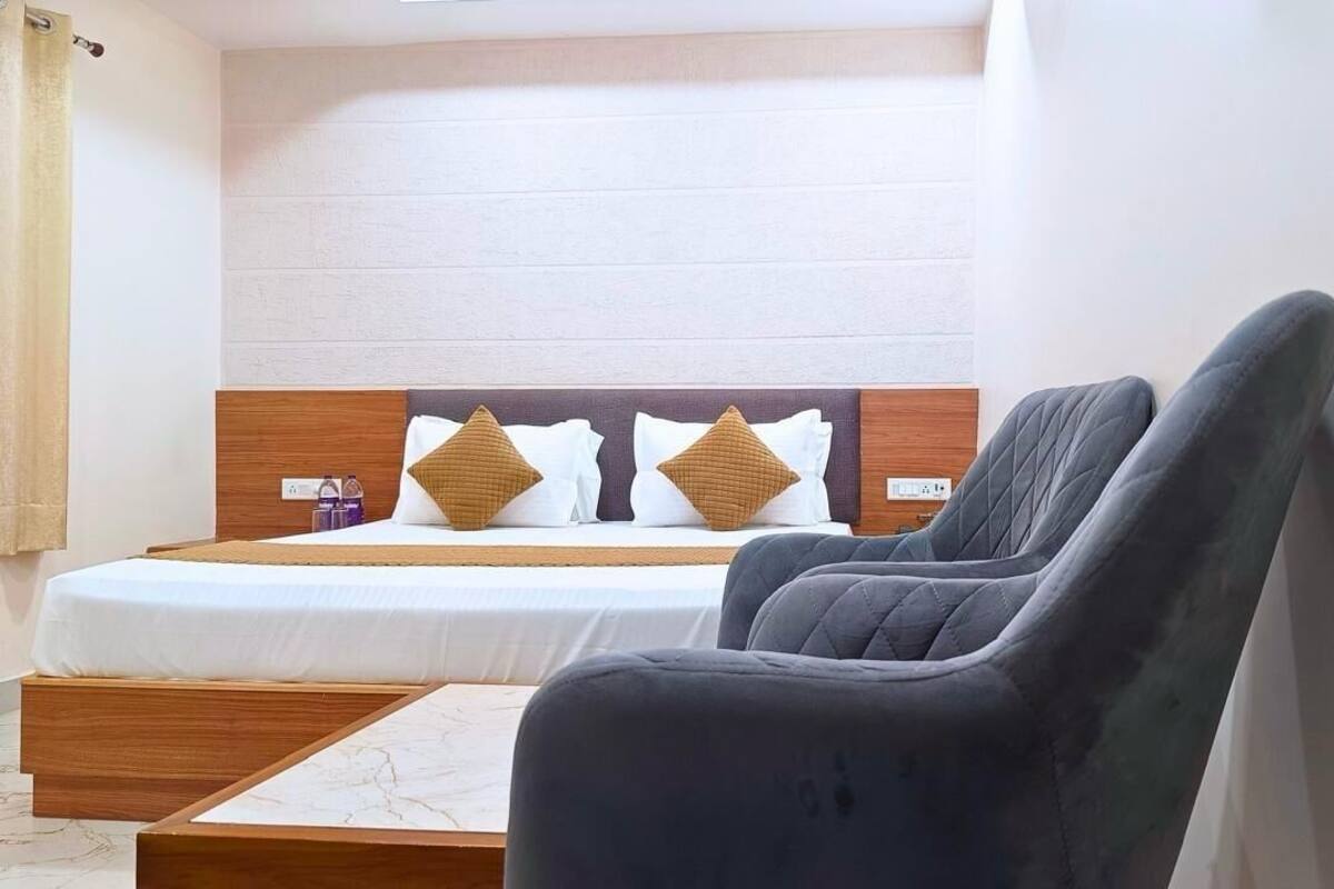 A hotel room with a bed, two pillows, a nightstand, a chair, and a small table.