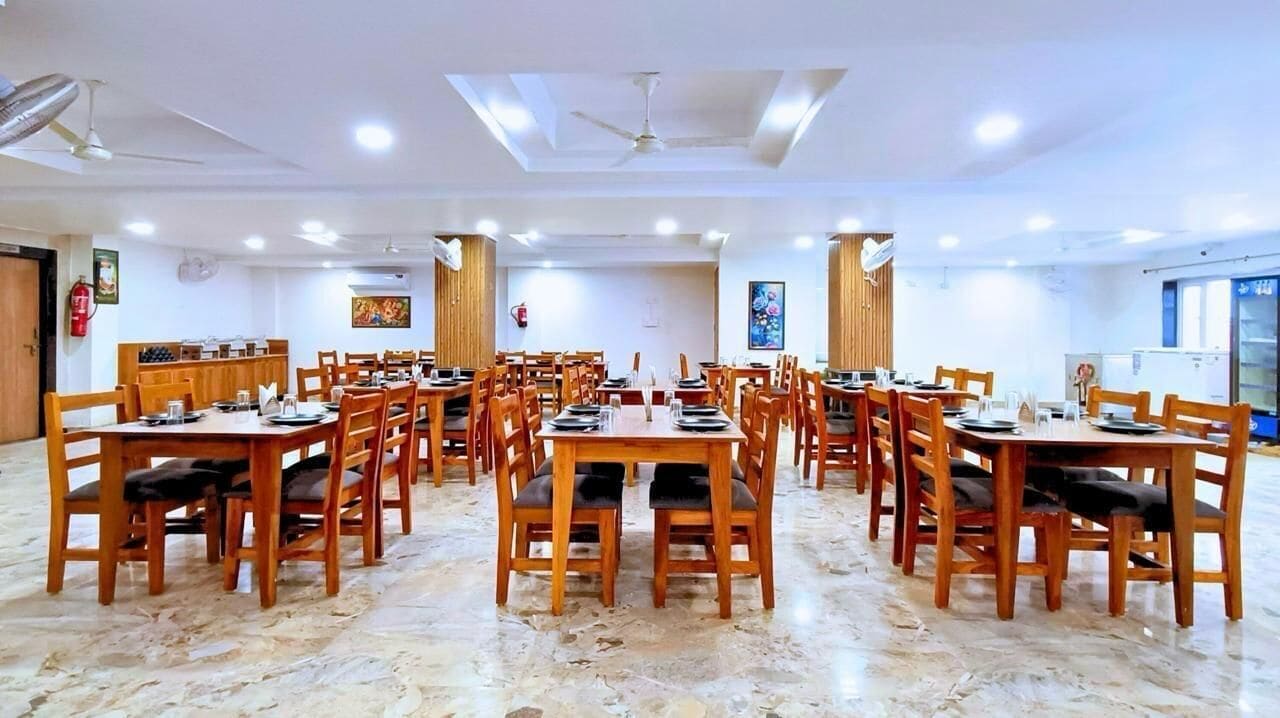 A spacious dining area with multiple wooden tables and chairs, ceiling fans, and air conditioning units.
