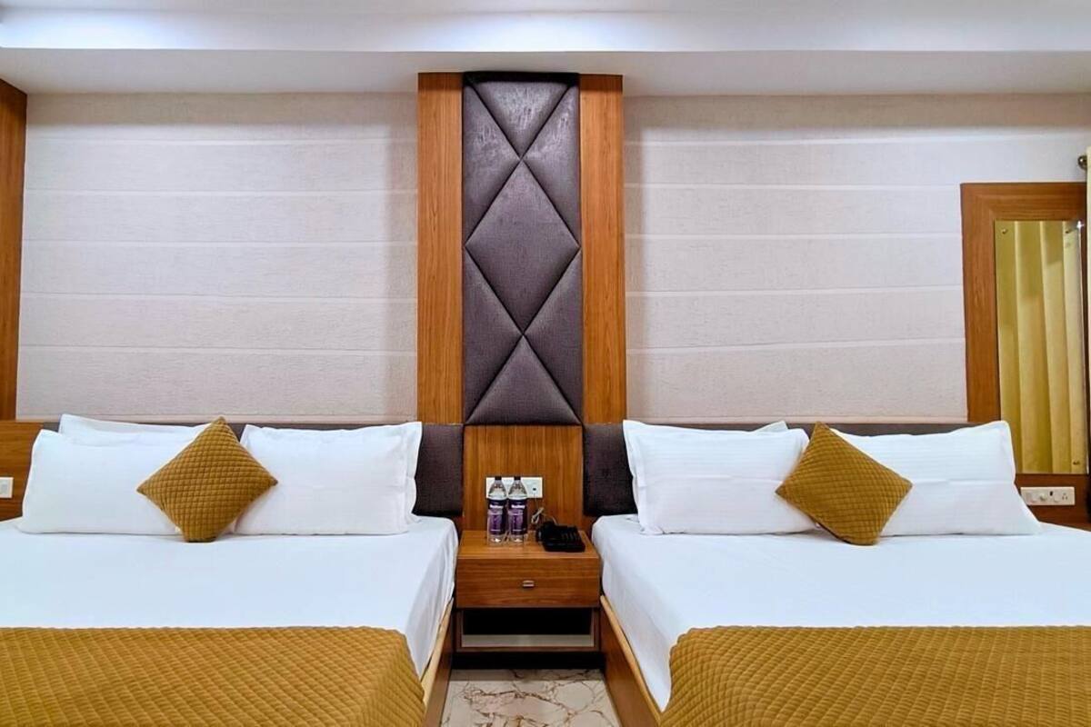 A hotel room with two beds, a wooden headboard, a nightstand with bottles, and a mirror.