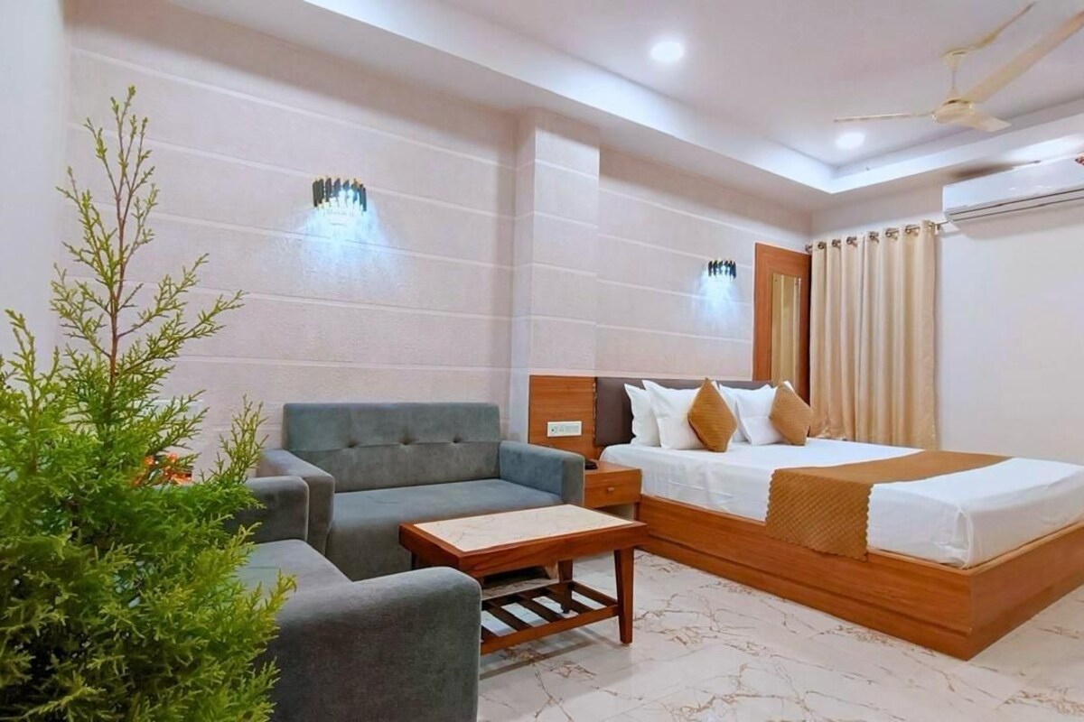 A hotel room with a bed, a sofa, a small table, and a potted plant.
