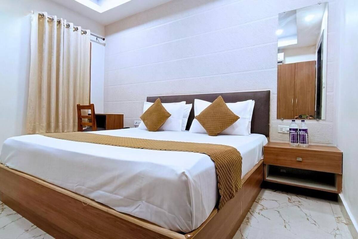 A neatly made bed with a wooden frame and white bedding, a bedside table with a mirror, and a window with curtains.