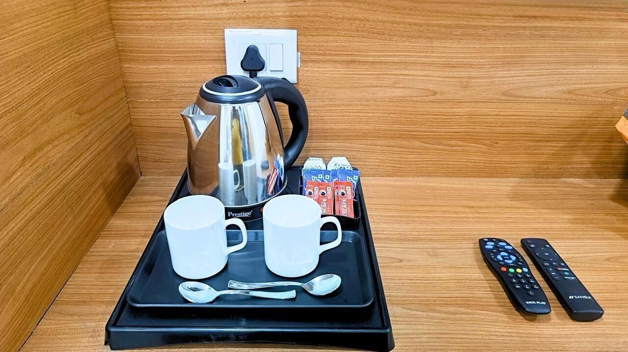 Una bandeja con una tetera, tazas, una cuchara y controles remotos sobre un piso de madera.