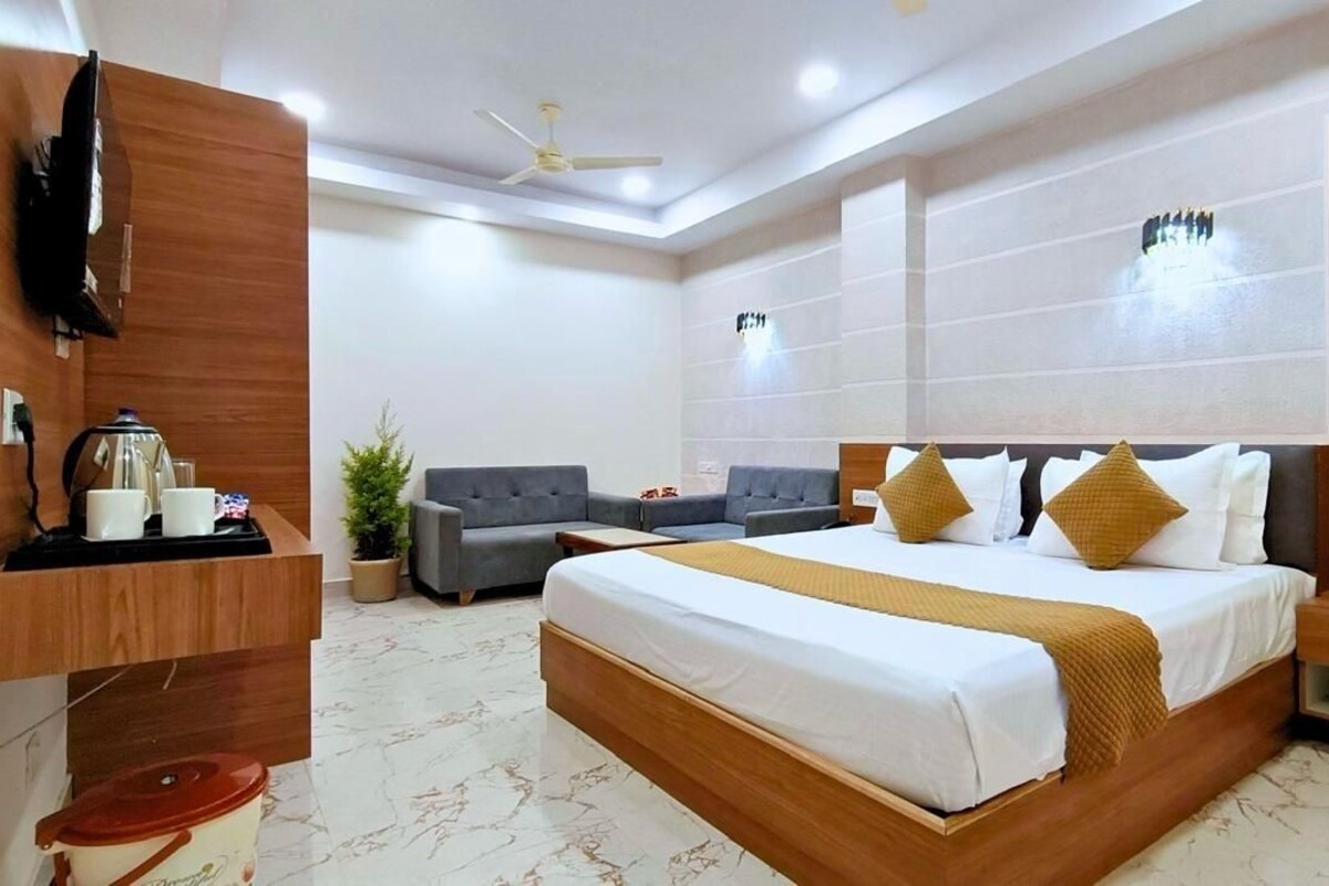 A hotel room with a large bed, a desk with a coffee maker, a TV, and a seating area with two sofas.