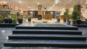 Eine Hotelhalle mit Marmorboden, einer Rezeption, mehreren Blumentöpfen und einer Treppe, die in die obere Etage führt.