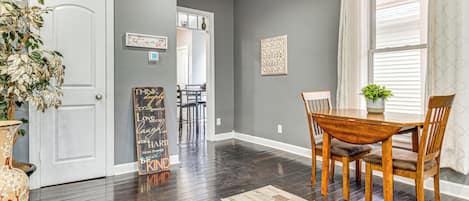 A dining area with a wooden table and chairs, a rug, and a potted plant.