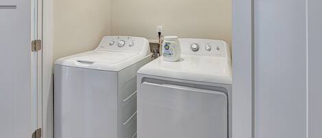 Une buanderie avec deux machines à laver à chargement frontal blanches, et une bouteille de lessive posée sur la machine de droite.