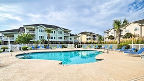 A swimming pool area with blue lounge chairs, a white fence, and multi-story buildings in the background. - < 5 Mi to Private Beach Access! Myrtle Beach Condo (Myrtle Beach)