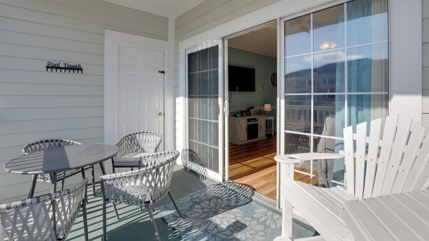 A patio with a table and chairs, a sliding glass door leading to an interior space, and a sign for pool towels. - < 5 Mi to Private Beach Access! Myrtle Beach Condo (Myrtle Beach)