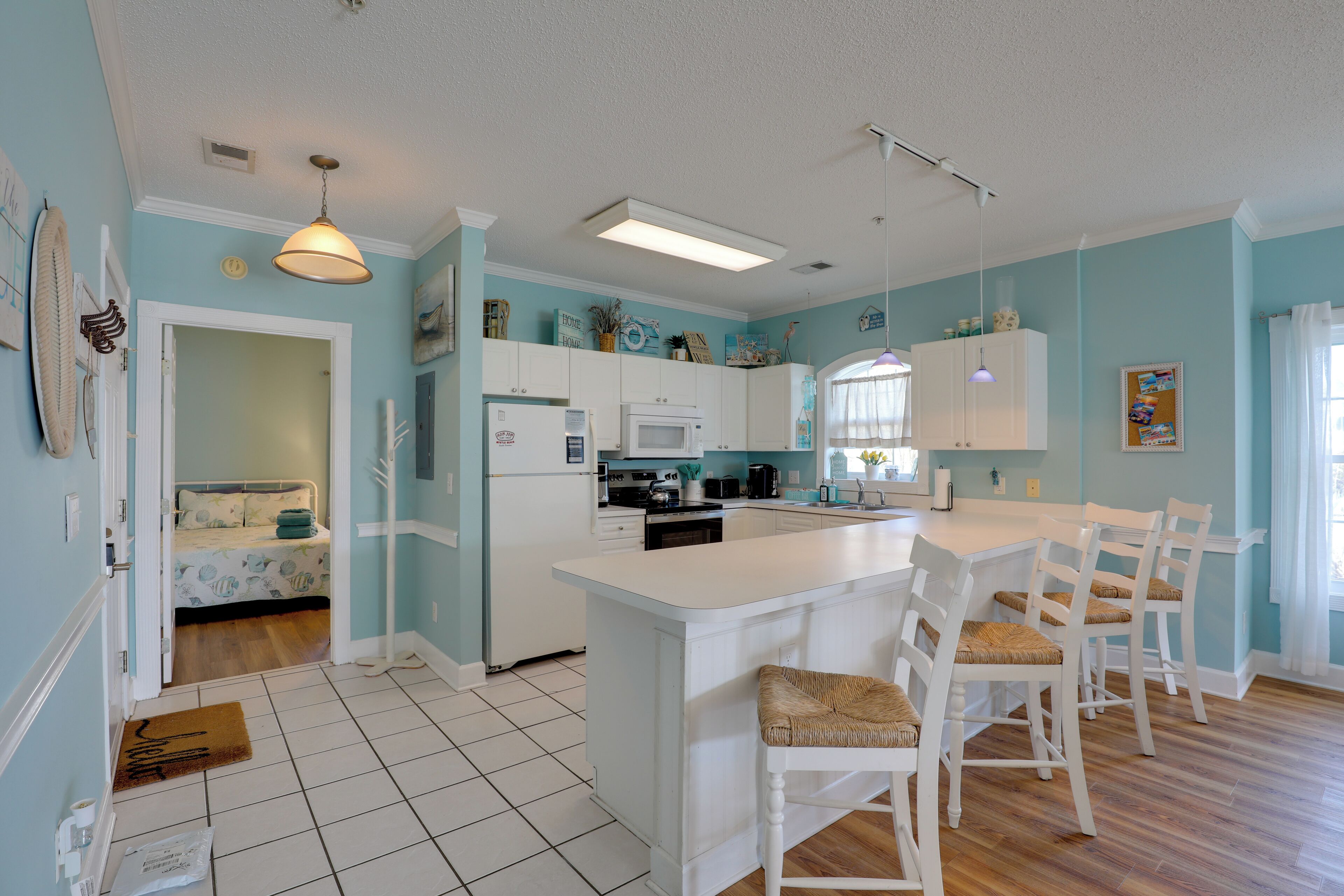 A kitchen with white cabinets, a central island with bar stools, a microwave, and a refrigerator.