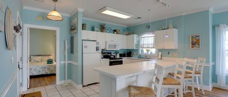 A kitchen with white cabinets, a central island with bar stools, a microwave, and a refrigerator.