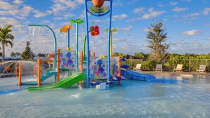 Een waterpark met glijbanen, een waterspeelplaats en ligbedden bij het zwembad.