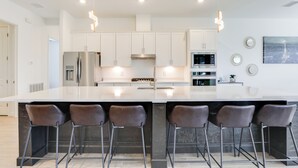 Een moderne keuken met een groot eiland, roestvrijstalen apparatuur en barstoelen.