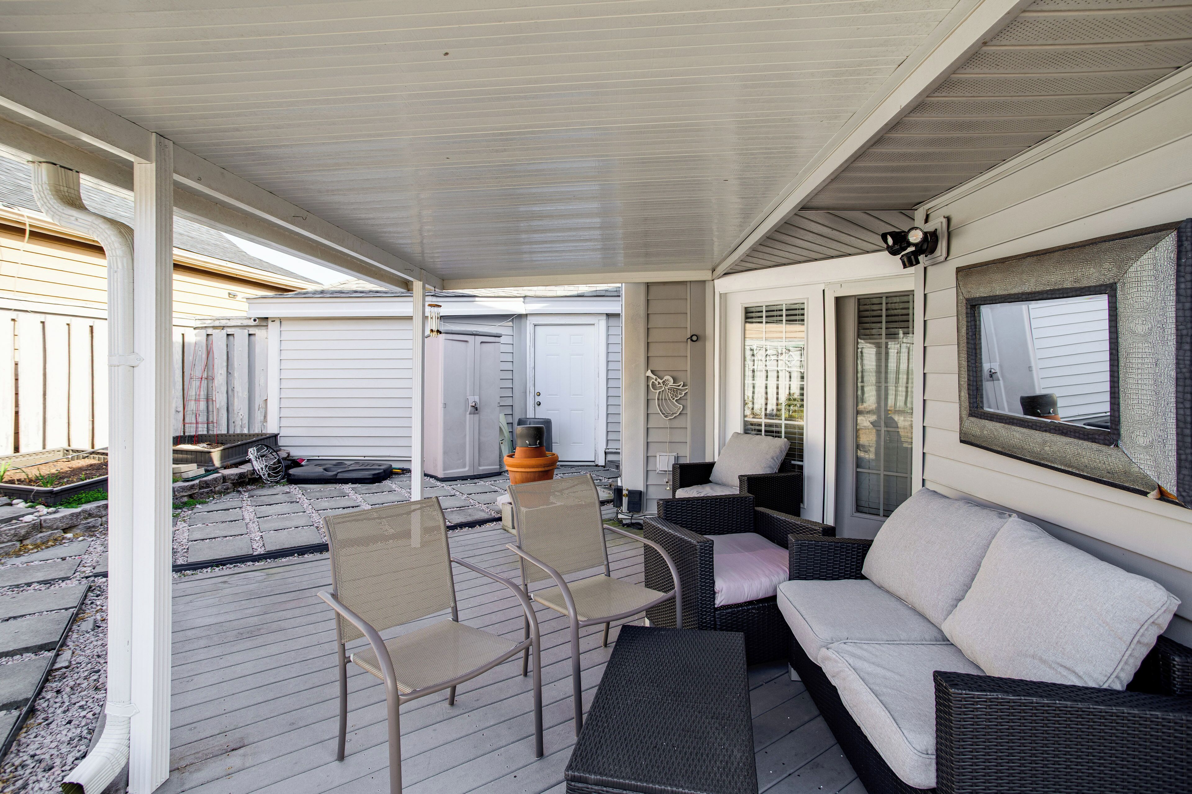 A covered patio area with outdoor furniture, including chairs and a sofa, and a large mirror on the wall.