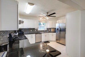 A modern kitchen with white cabinets, a black countertop, stainless steel appliances, and a ceiling fan. - Private Yard & Gym: Classic Columbia Home (Columbia)