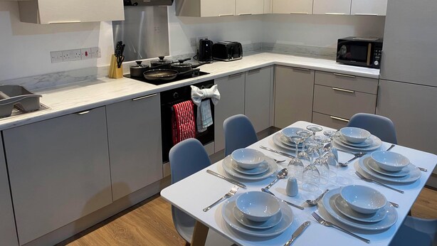 Une cuisine moderne avec un coin repas aménagé pour accueillir six personnes. Elle comprend une cuisinière, un four à micro-ondes et un évier.