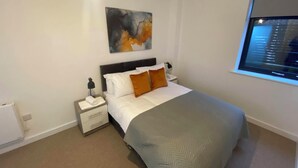 Une chambre à coucher bien rangée, avec un lit, des tables de chevet, une commode, un tableau abstrait accroché au mur et une fenêtre donnant sur un beau paysage.