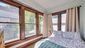 A bedroom with a wooden floor, a bed with floral bedding, and a window with curtains. - Walk to Colorado College & Dwtn! Home w/ Patio (Colorado Springs)