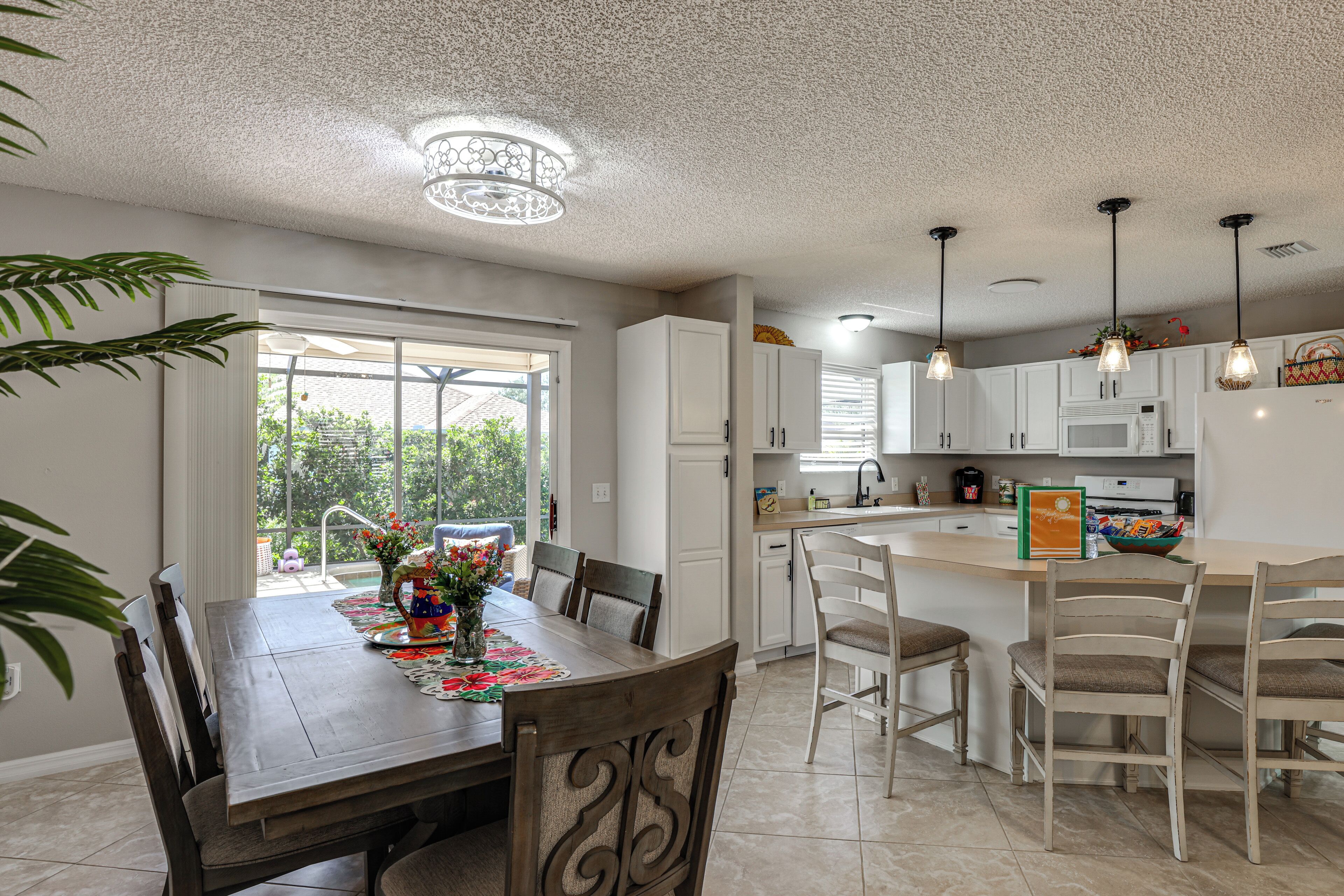 A modern kitchen with white cabinets, a central island, pendant lighting, and a dining area with a wooden table and chairs.