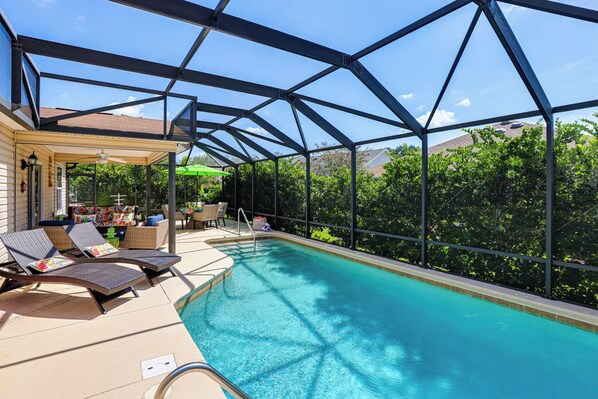 Une piscine entourée de parois en verre, des chaises longues et un espace patio couvert.