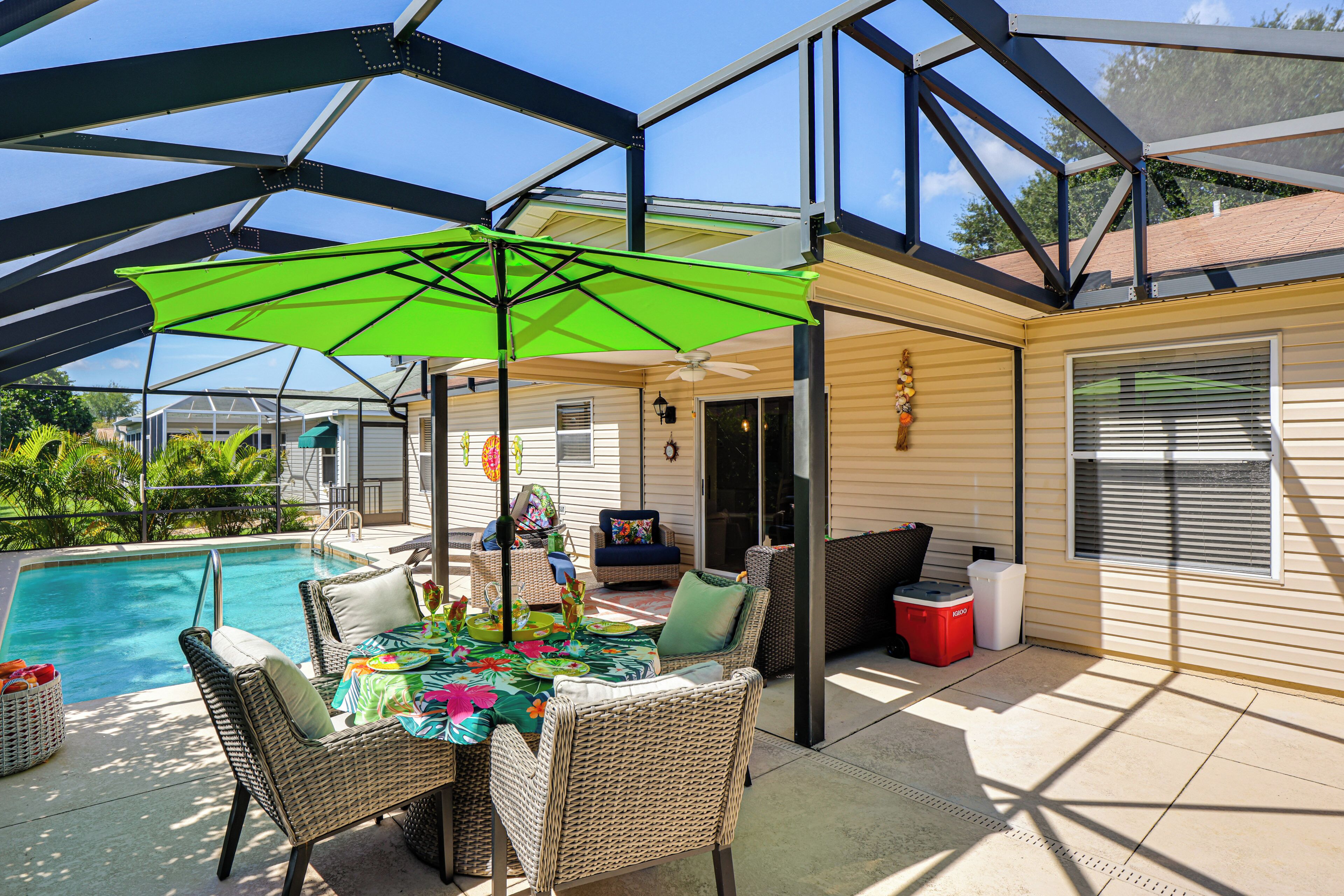 A covered outdoor area with a pool, wicker furniture, and a table set for dining.
