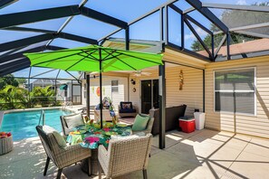 Un espacio al aire libre cubierto con piscina, mobiliario de mimbre y una mesa lista para comer.