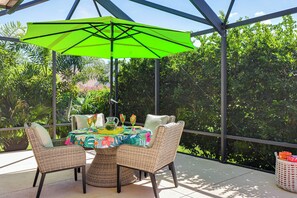 Une terrasse extérieure avec une table dressée pour deux personnes, entourée de chaises en osier, sous un parasol vert.