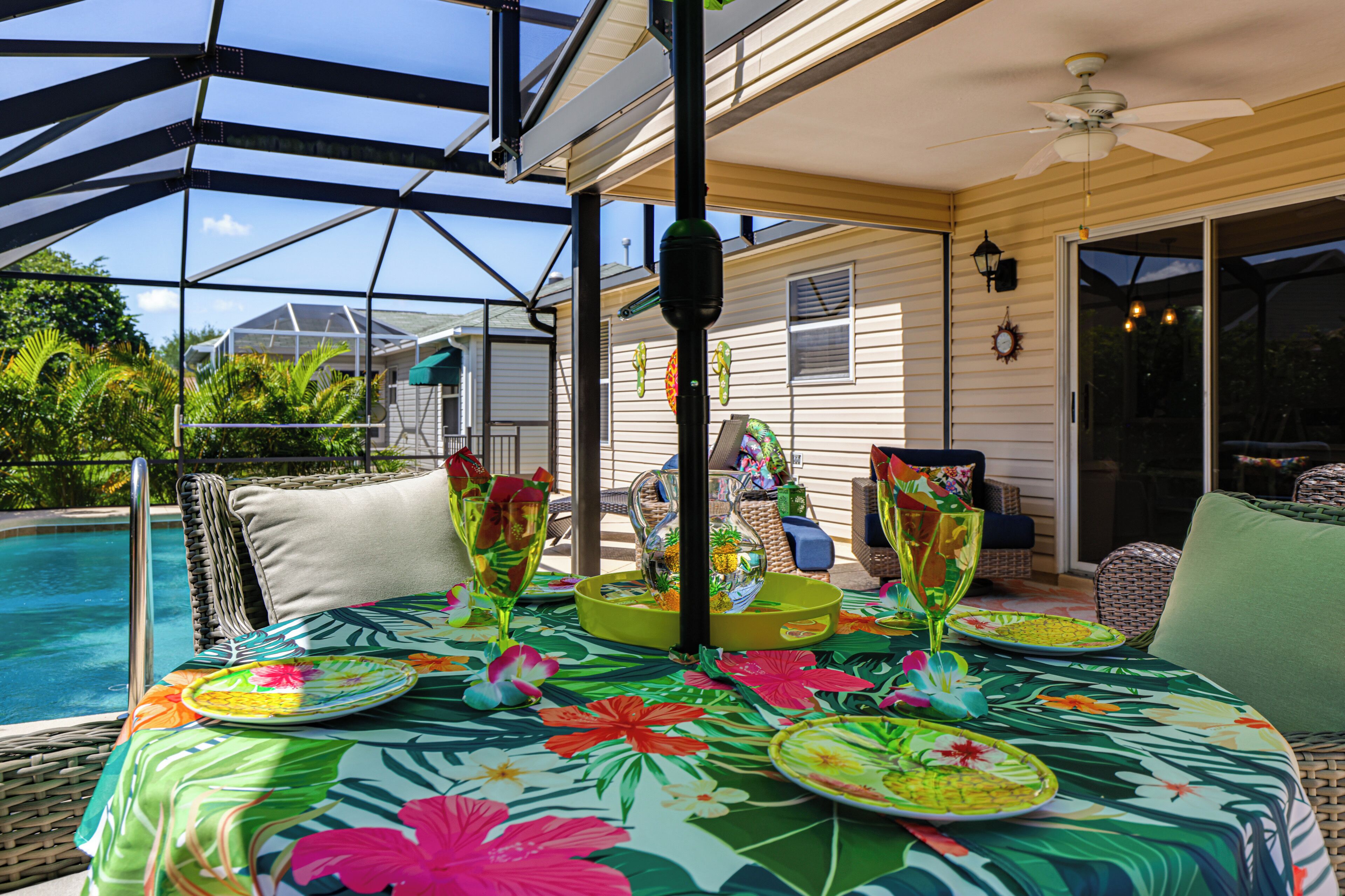 A covered outdoor seating area with a pool, wicker furniture, and a table set with tropical tableware.