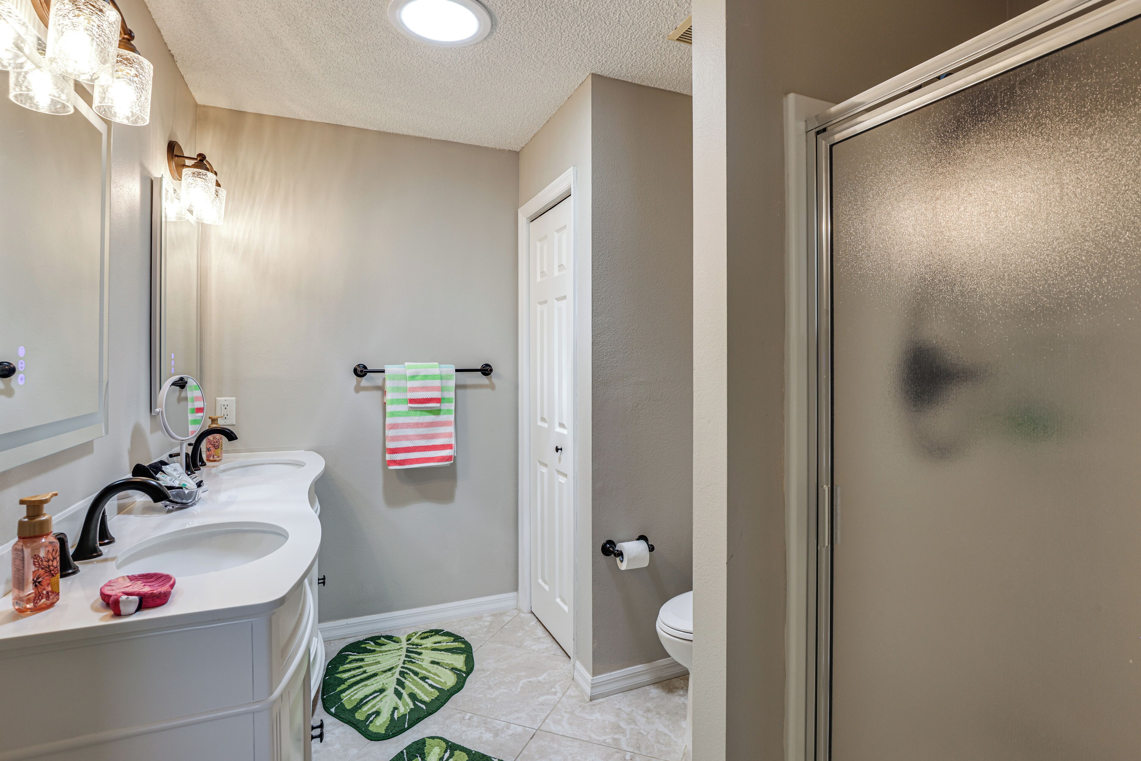 A bathroom with a white sink, a mirror, a towel rack with a striped towel, a toilet, and a shower door.