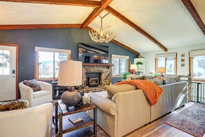 A spacious living room with a fireplace, comfortable seating, and a large window providing natural light. - Hike, Bike & Ski: Evergreen Home w/ Game Room! (Evergreen)