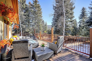 A deck with wicker furniture, potted plants, and a view of snow-covered trees. - Hike, Bike & Ski: Evergreen Home w/ Game Room! (Evergreen)