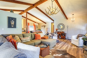 A spacious living room with a sectional sofa, a coffee table, and a cowhide rug. There is a chandelier, a mirror, and a bookshelf in the room. - Hike, Bike & Ski: Evergreen Home w/ Game Room! (Evergreen)
