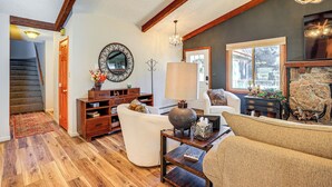 A spacious living room with hardwood floors, a fireplace, a chandelier, and a large window. - Hike, Bike & Ski: Evergreen Home w/ Game Room! (Evergreen)