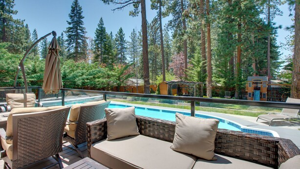 Un espace aménagé au bord de la piscine, avec des meubles en osier et une vue sur la piscine et la forêt.