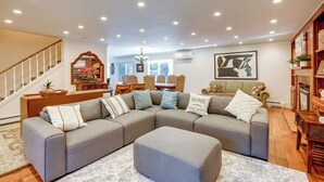 Un salon spacieux avec un grand canapé d’angle, un coin repas avec des meubles en bois et un escalier doté de rampes blanches.