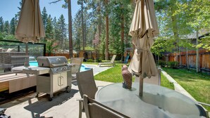 Une terrasse extérieure équipée d’un barbecue, de chaises longues et d’une table en verre.